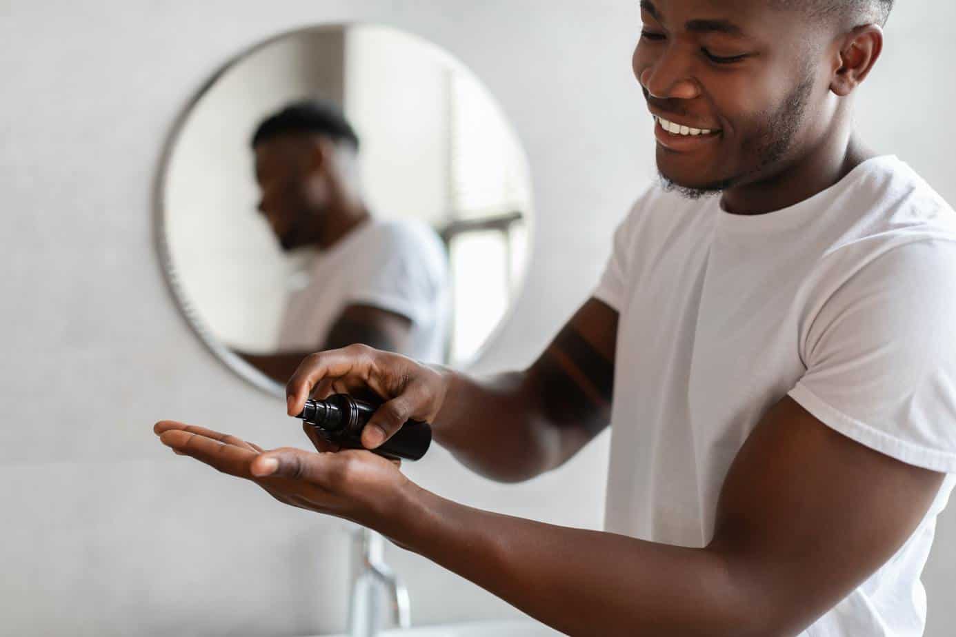 Black Man Squeezing Bottle Caring For Facial Skin In Bathroom