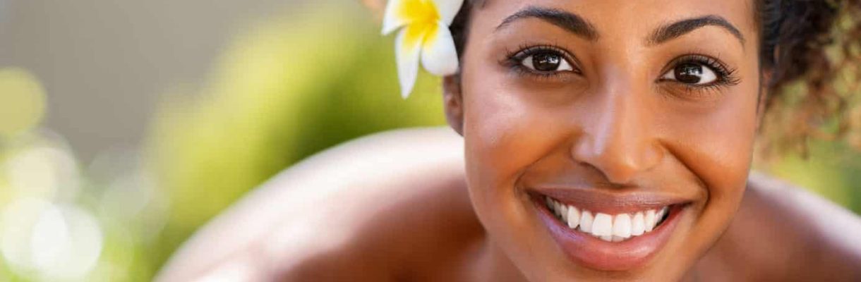 Closeup face of young african american woman in a wellness center ready for massage therapy. Portrait of beautiful girl lying down on massage table at spa resort. Smiling girl looking at camera while awaiting beauty treatment.